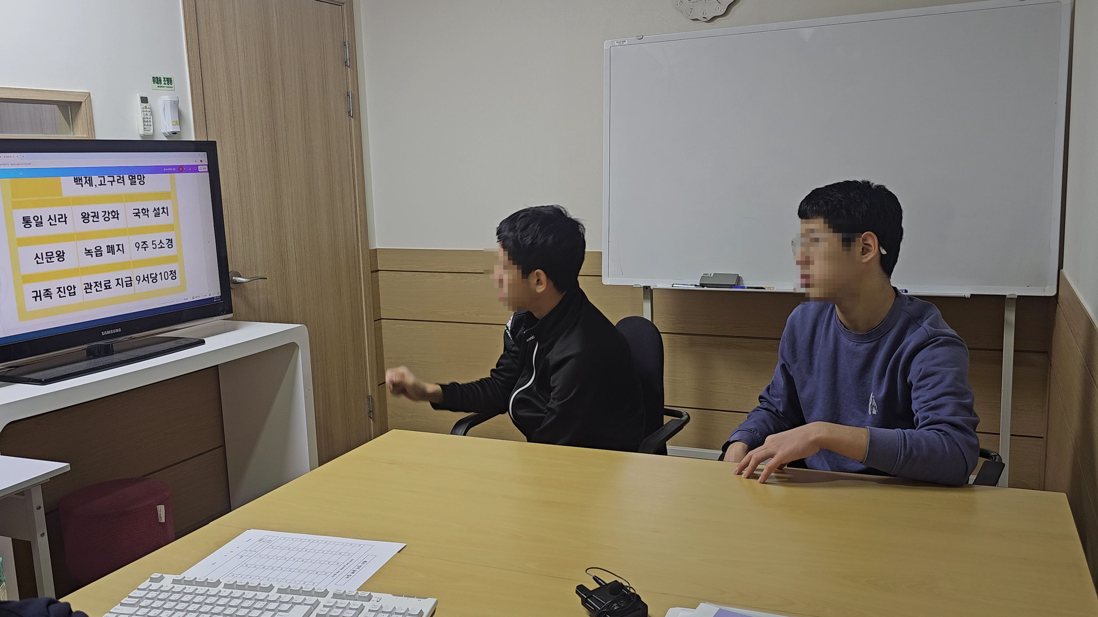 두비전 기존 수업에서 두 학생이 화면이 놓인 테이블에 앉은 장면. 여러 학생이 자료를 함께 보는 환경을 참고할 수 있습니다.